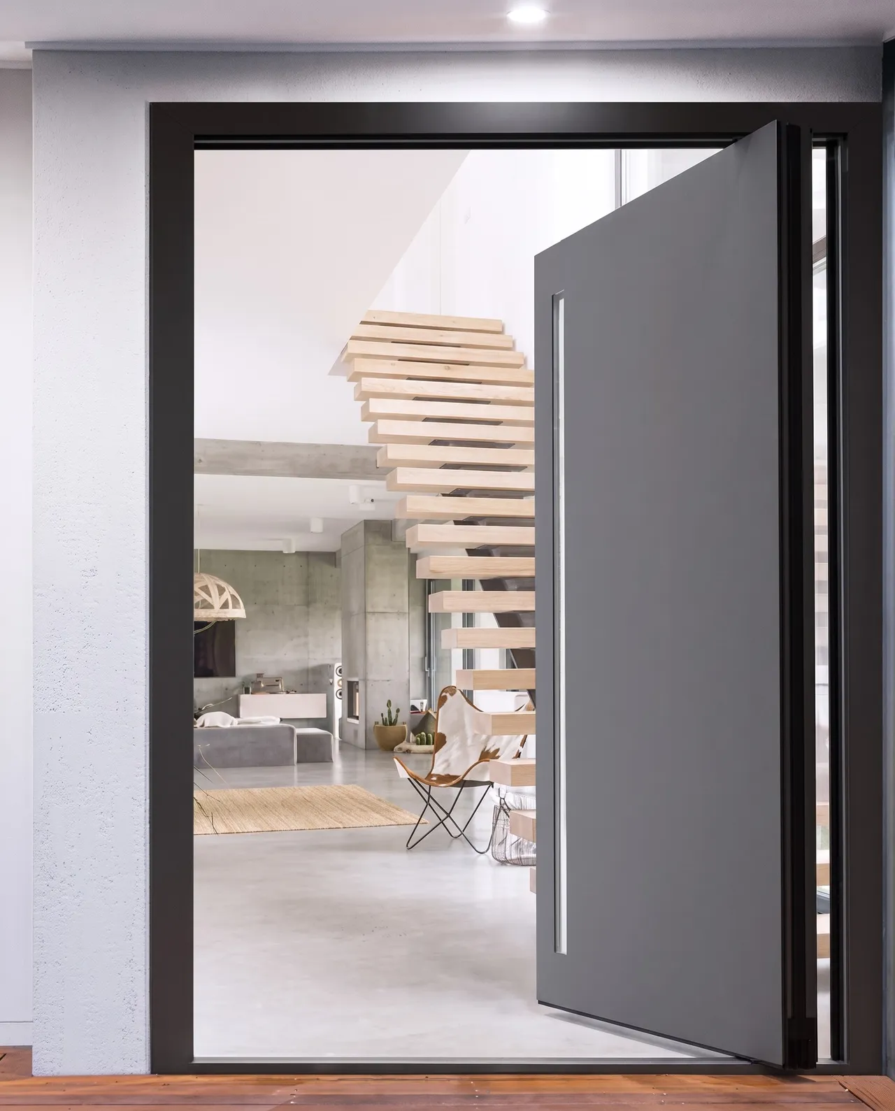 Une grande porte pivotante ouverte sur un hall et un escalier suspendu
