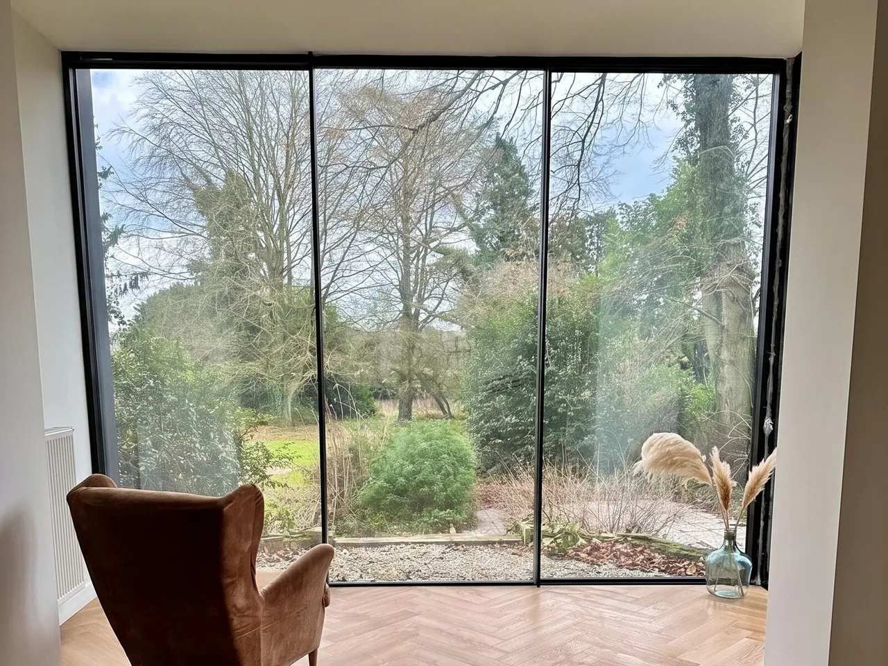 Living room of the Ellie house in Brussels: a three-panel minimalist sliding bay opening onto a wooded garden